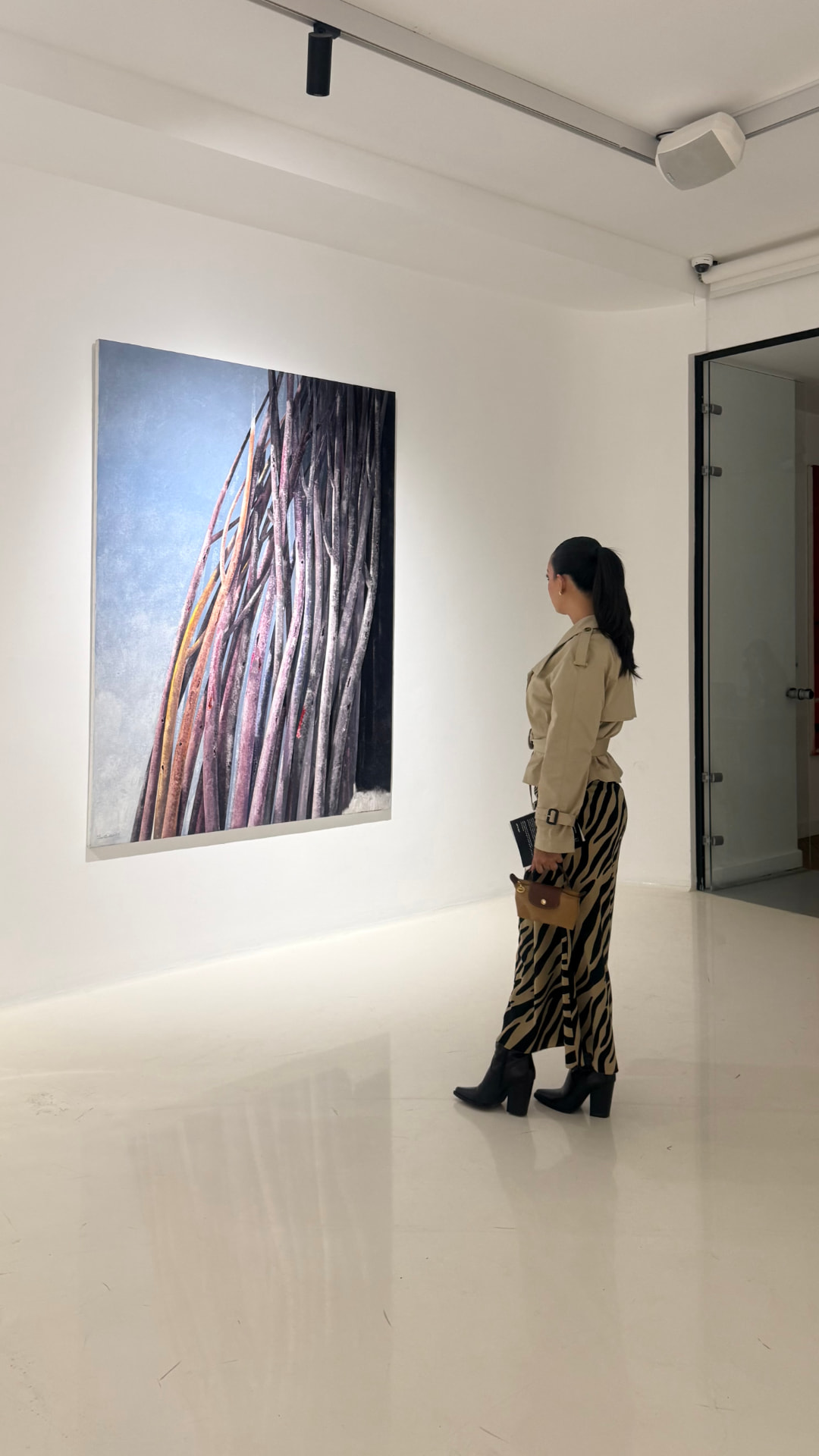 Model in a belted beige trench coat and zebra-print skirt viewing a painting in a gallery