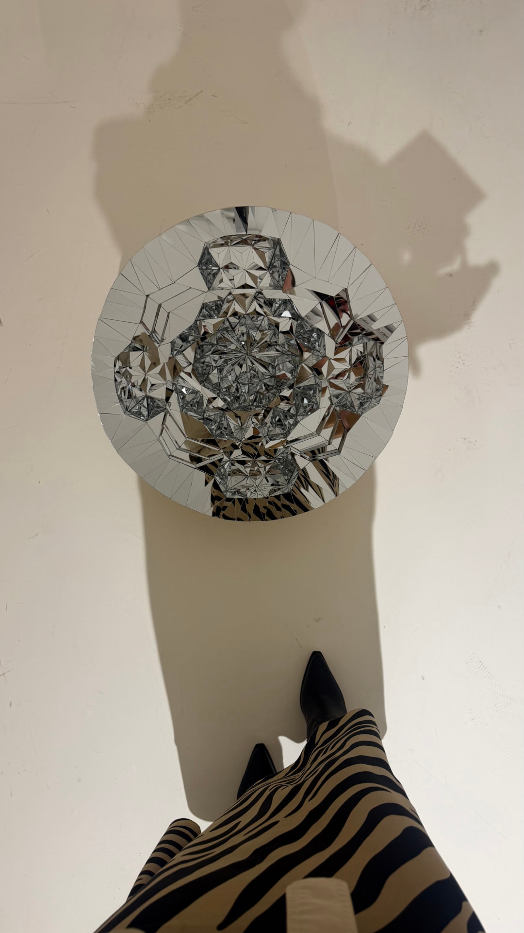 Model's black boots and zebra-print skirt beside a faceted circular mirror artwork